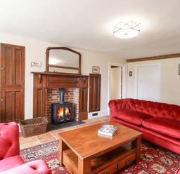 A living room with red sofas wooden coffee table fireplace and television at West House Farm in Leiston