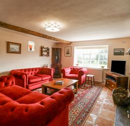 A living room with red sofas wooden coffee table grandfather clock and television at West House Farm in Leiston