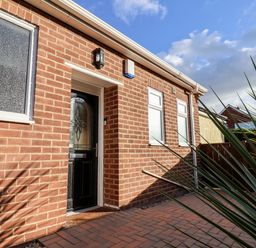 The exterior of a brick house with a black door and three windows beside a paved pathway at Meadowfields in Whitby