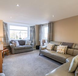 A living room with two sofas a wooden cabinet lamps and plaid curtains at Meadowfields in Whitby