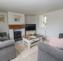 A living room with two grey sofas a wooden coffee table a small fireplace and a television at Alices Cottage in Burton Bradstock
