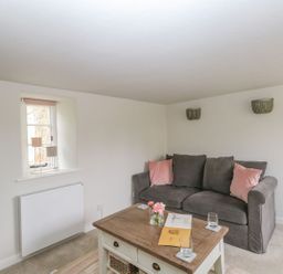 A sitting room with a grey sofa and pink cushions next to a wooden coffee table and a television at Alice's Cottage in Burton Bradstock