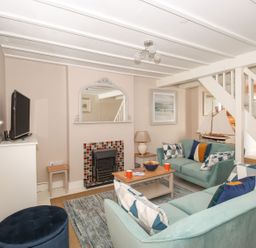 A living room with two teal sofas a wooden coffee table a fireplace and a television at Little Gull Cottage in Weymouth