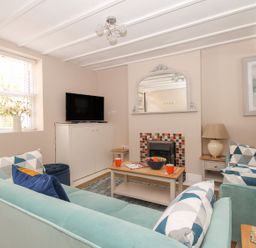 A living room with two sofas a coffee table a TV on a cabinet a mirror above a fireplace and a window with flowers at Little Gull Cottage in Weymouth