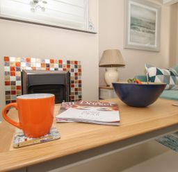 A living room with a wooden coffee table holding orange mugs magazines and a bowl in front of a fireplace at Little Gull Cottage in Weymouth