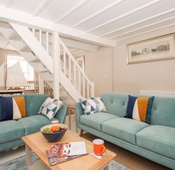 A living room with two teal sofas and a coffee table with fruit bowl and mugs at Little Gull Cottage in Weymouth