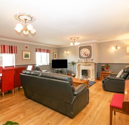 A living room with black leather sofas a wooden coffee table a piano and a dining table with red chairs at Tyn Rallt Ice Cream Farm Malltraeth near Newborough