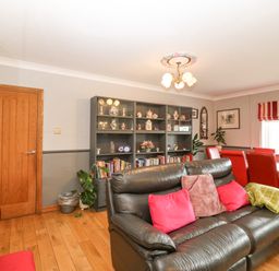 A living room with a black leather sofa with cushions a dining table with red chairs and a bookshelf with decorative items at Tyn Rallt Ice Cream Farm Malltraeth near Newborough