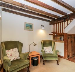 A sitting area with two green armchairs a small table and a lamp under wooden ceiling beams at Well Cottage in Moreton-In-Marsh