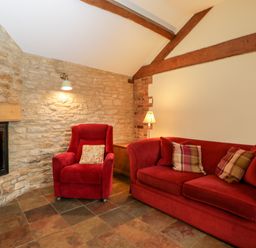 A living room with a red sofa and armchair beside a stone fireplace at Stable Cottage in Moreton-In-Marsh