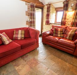 A sitting area with two red sofas and plaid cushions near windows with plaid curtains at Stable Cottage in Moreton-In-Marsh