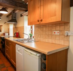 A kitchen with wooden cabinets a sink a dishwasher a mini fridge and a stove at Stable Cottage in Moreton-In-Marsh