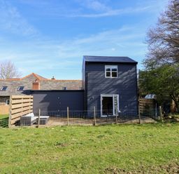 A fenced patio with outdoor seating and a two-story house with a slate roof and wooden walls at The Stables in Tafarn-Y-Gelyn