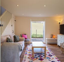 A living room with a sofa a chair a coffee table a television and an open door showing a grassy field at The Stables in Tafarn-Y-Gelyn