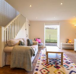 A living room with a sofa near stairs a coffee table and a television at The Stables in Tafarn-Y-Gelyn