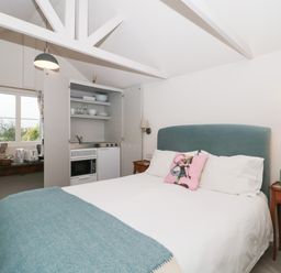 A bedroom with a bed a kitchenette and a table under a window at The Potting Shed in Combe near Langport