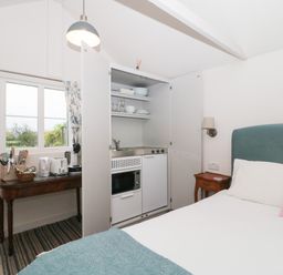 A bedroom with a built-in kitchenette cupboard and a small wooden table with kitchen appliances at The Potting Shed in Combe near Langport