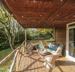 A wooden deck with wicker furniture and string lights overlooking trees at Pear Tree Lodge in Combe near Langport