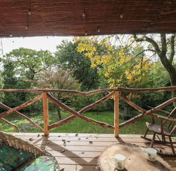 A porch with a wooden rocking chair wicker chair a wooden table with two mugs and a garden view at Pear Tree Lodge in Combe near Langport