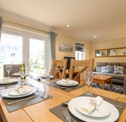 A dining table set with plates glasses and napkins next to a living area with sofas a coffee table and wall decorations at Manuka in Falmouth