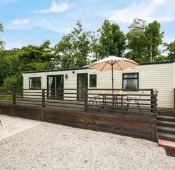 A mobile home with a wooden deck table and chairs with umbrella in front at Little Malory in St Giles-On-The-Heath