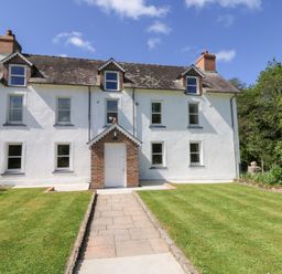 A white two-story house with a brick entrance and a tiled roof with dormer windows and a lawn in front at Glanduad Fawr in Newport Pembrokeshire