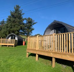 Two small cabins with wooden decks on green grass near trees at Tarrenhendre Pod in Llanegryn near Tywyn