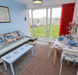 A living room with sofa table and dining table near large glass doors with a view outside at Culver View in Sandown