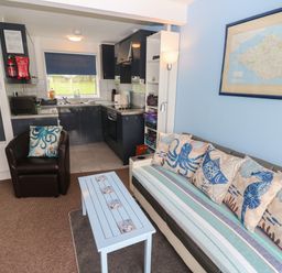 A living room with a sofa and cushions next to a blue wall with a map and an armchair facing a blue coffee table at Culver View in Sandown