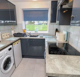 A kitchen with grey cabinets a washing machine a refrigerator a sink and an electric stove at Culver View in Sandown