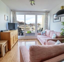 A living room with pink sofas facing a wooden cabinet with a tv and glass doors at Branwen in Porthmadog