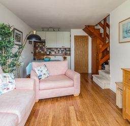 A living room with pink sofas and pillows a wooden floor a kitchen area with cabinets and a dining table and wooden stairs at Branwen in Porthmadog