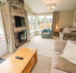 A living room with two beige sofas a blue armchair a wooden coffee table a wall-mounted tv and a fireplace at Lakeside 12 in Carnforth