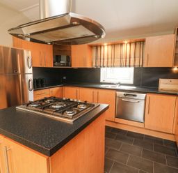 A kitchen with wooden cabinets a black countertop gas stove dishwasher and stainless steel refrigerator at Lakeside 12 in Carnforth