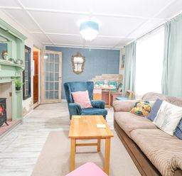 A living room with a beige sofa and blue armchair next to a wooden coffee table and green fireplace at White Rabbit Cross Lane in Eccles On Sea