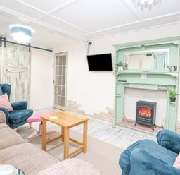 A sitting room with blue armchairs a beige sofa a wooden coffee table a green fireplace mantel and a wall-mounted television at White Rabbit Cross Lane in Eccles-On-Sea