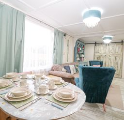 A dining table set with plates cups and utensils next to a living room with blue armchairs a sofa and a cabinet at White Rabbit Cross Lane in Eccles-On-Sea