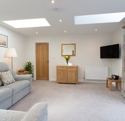 A living room with sofas a wooden cabinet and a wall mounted television at Cornish Views in Camborne