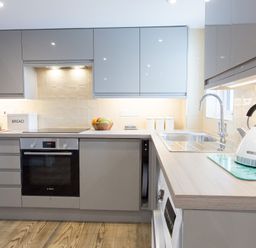 A kitchen with grey cabinets a built-in oven a stovetop a bread box a fruit bowl a kettle on the counter and a double sink at Cornish Views in Camborne