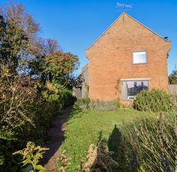 A brick house with two windows a grassy lawn and bushes under a clear blue sky at Mundays in Orford