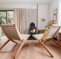 A living room with two woven wooden chairs facing a wood stove with a fire at Mundays in Orford