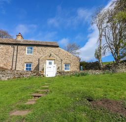 A stone house with a white gate and stone steps leading up to it surrounded by grass and trees at Swinhope View in Hexham