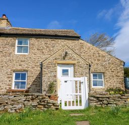 A stone house with a white wooden gate and grass in front at Swinhope View in Hexham