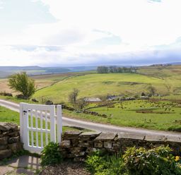 A white garden gate opening to a pathway with a stone wall and green fields with hills and trees in the background at Swinhope View in Hexham