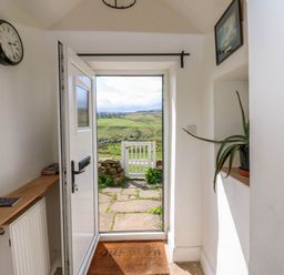 A hallway with an open door showing a stone path and green fields outside at Swinhope View in Hexham