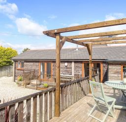 An outdoor wooden deck with a table and chairs and a pergola next to a wooden building at Lilys Pad in Okehampton