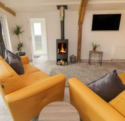 A living room with yellow sofas a wood burning stove and a wall mounted television at Windy Willows in Okehampton
