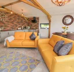A living room with yellow sofas a patterned rug and kitchen area with brick wall at Windy Willows in Okehampton