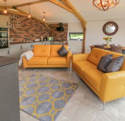 A living room with two mustard sofas grey and yellow rug open kitchen with brick wall and dining table at Windy Willows in Okehampton
