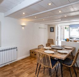A dining area with a wooden table set for four and wicker chairs next to a kitchen counter with a window at Sea Horses in Port Isaac
